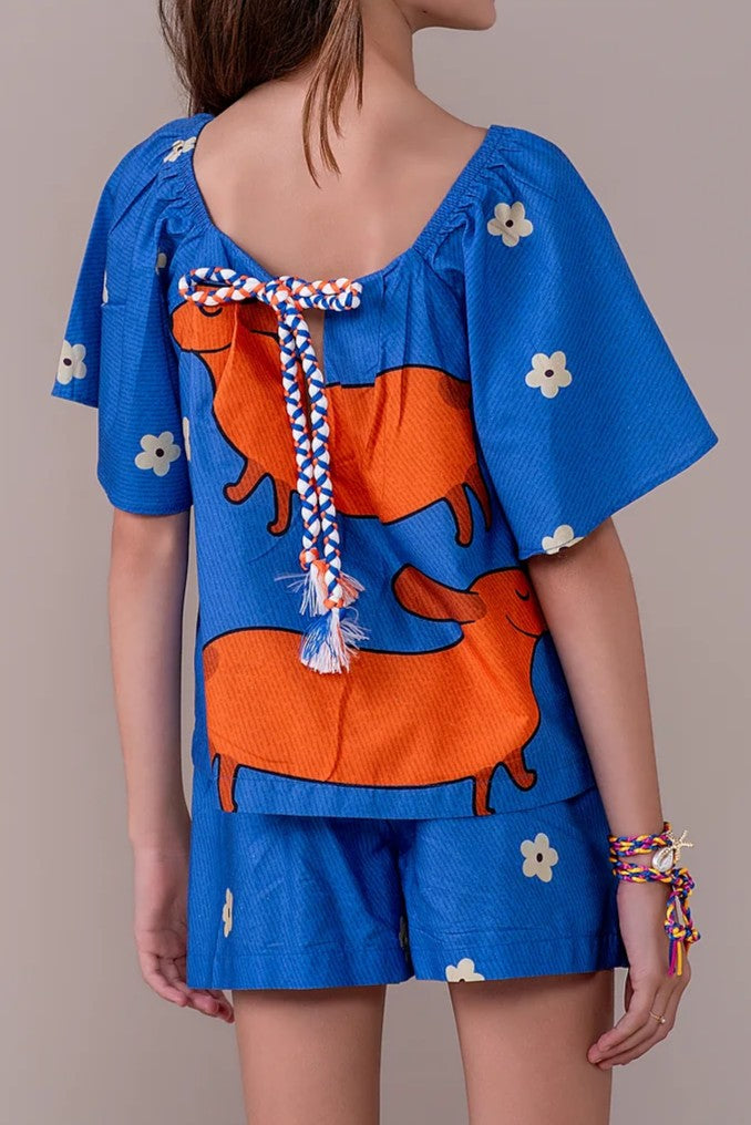 Conjunto infantil feminino com blusa azul de mangas bufantes e saia-short, estampa de cães salsichas e flores