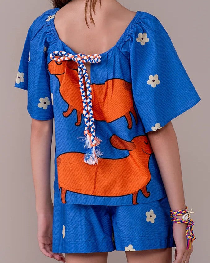 Conjunto infantil feminino com blusa azul de mangas bufantes e saia-short, estampa de cães salsichas e flores