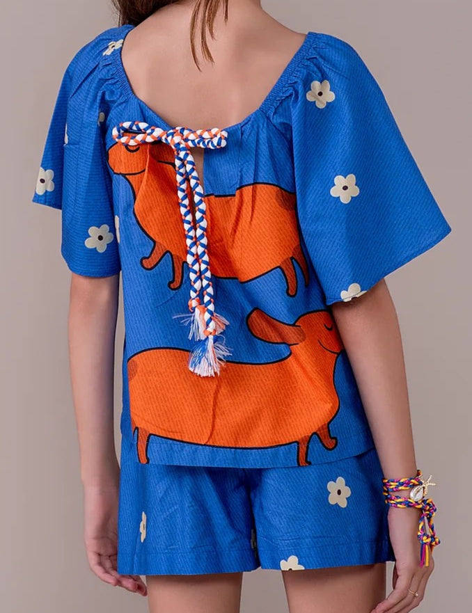 Conjunto infantil feminino com blusa azul de mangas bufantes e saia-short, estampa de cães salsichas e flores
