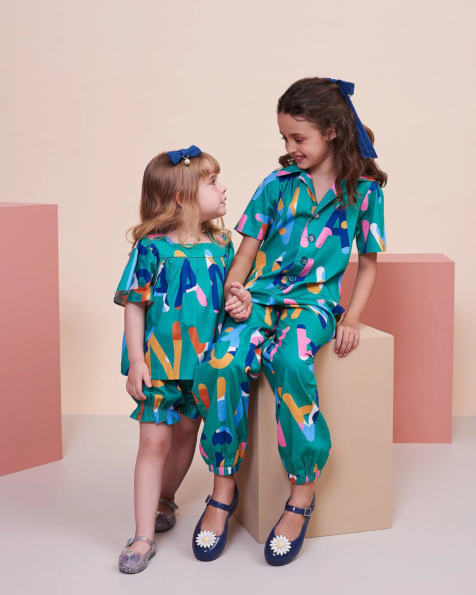 Macacao infantil feminino com padrão de letras coloridas em fundo azul e punhos ajustáveis