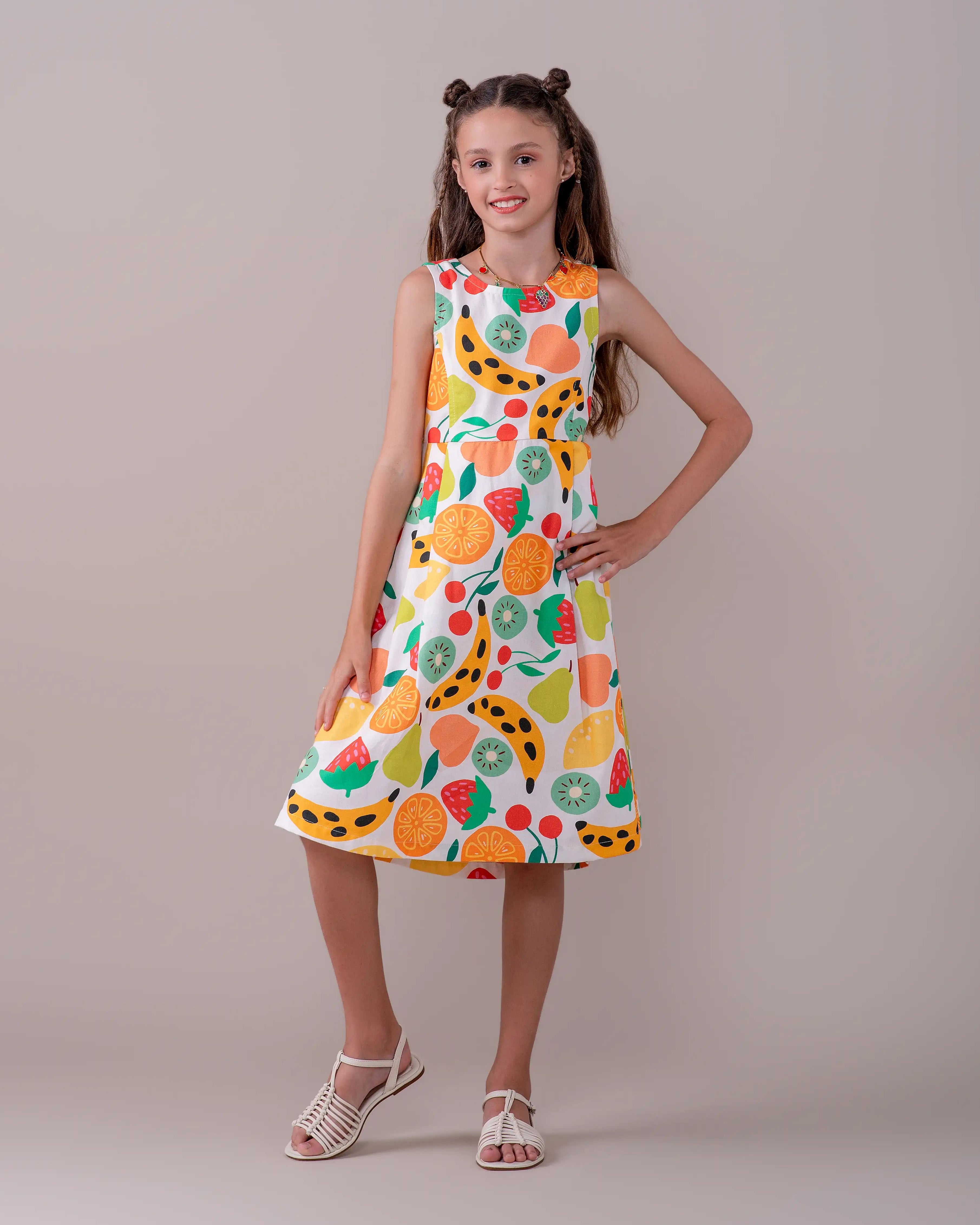Vestido feminino infantil com estampa de frutas coloridas em fundo claro, alças largas e saia solta