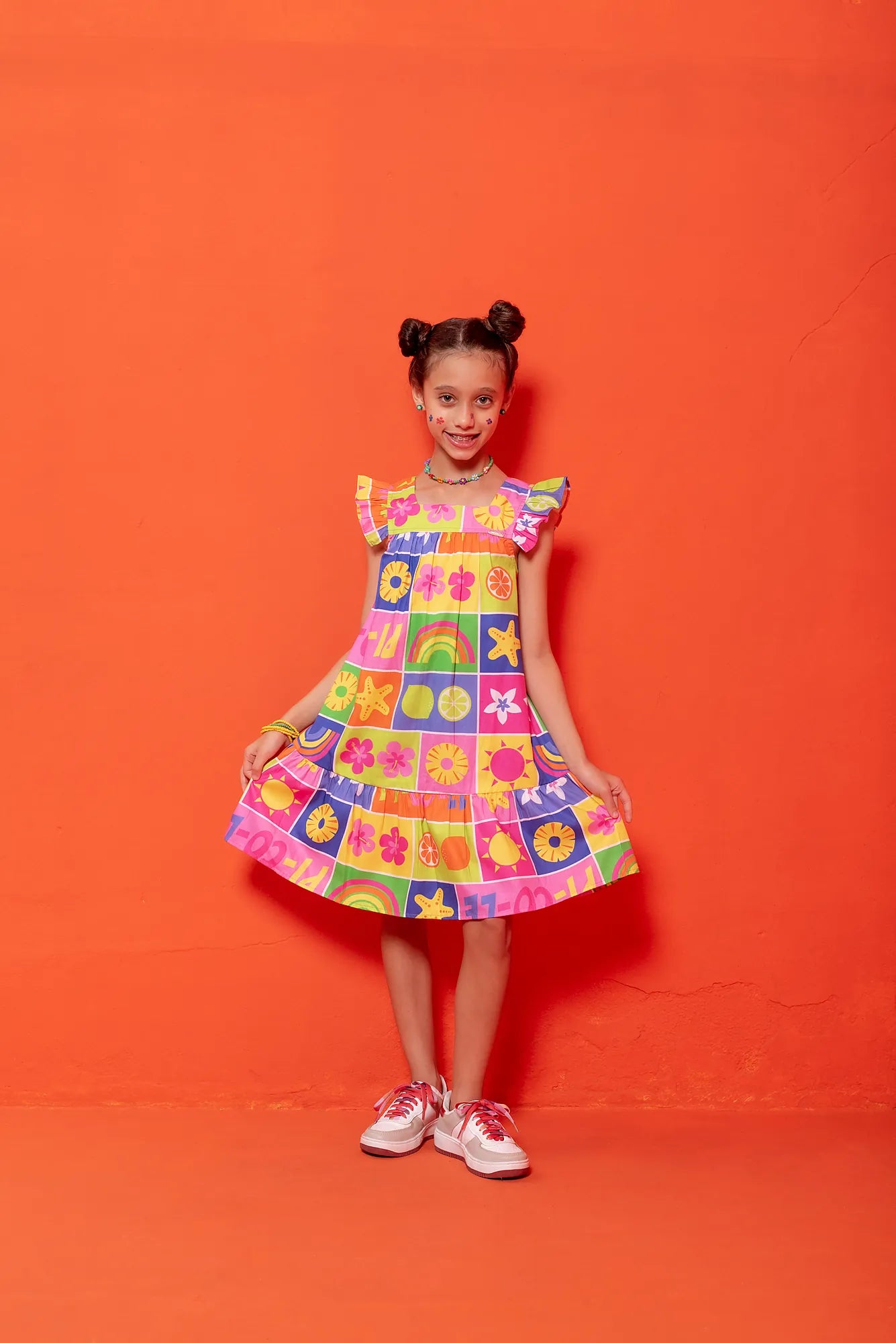 Vestido infantil com estampa colorida de flores e formas geométricas, alças largas e babados na barra