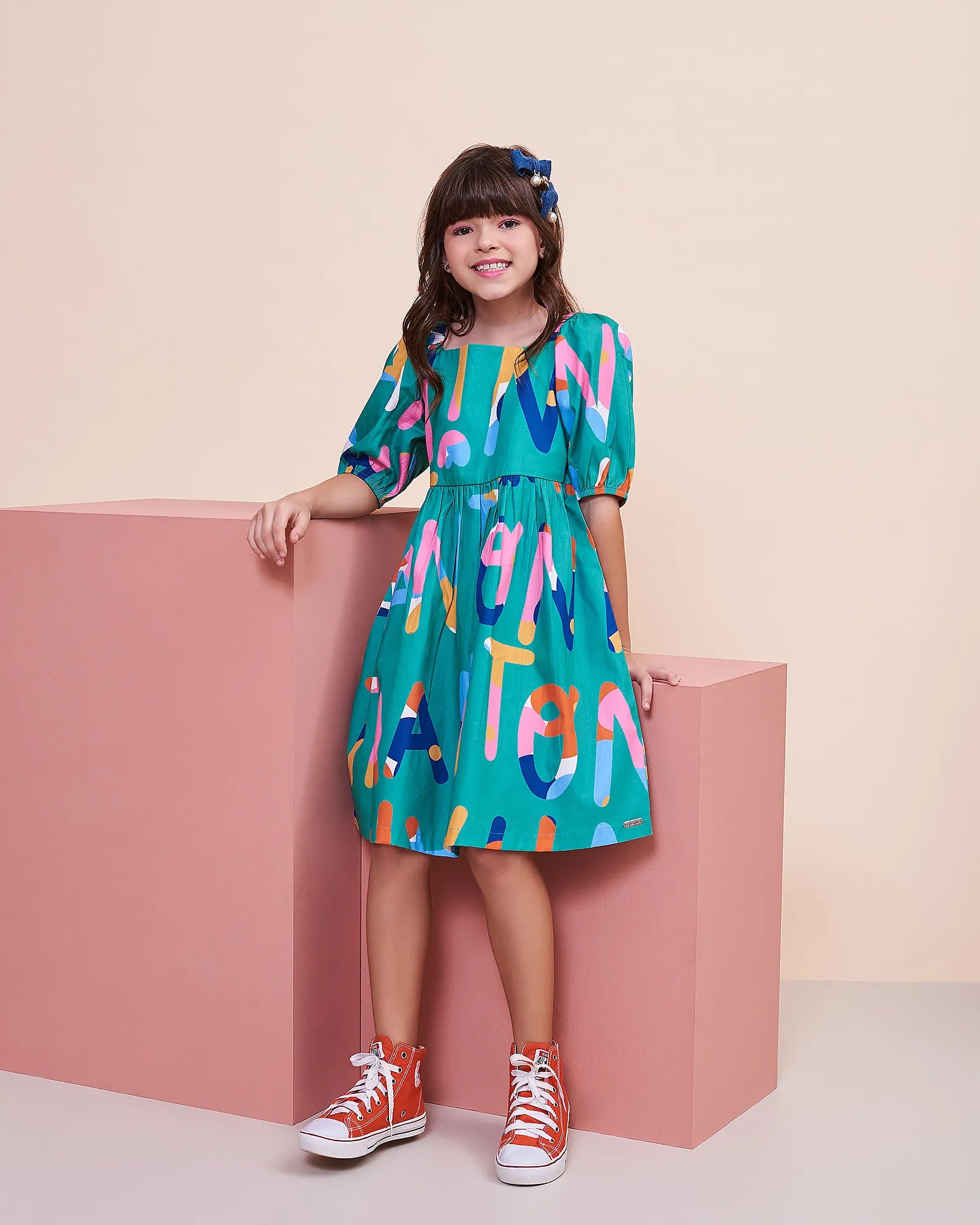 Vestido infantil com padrão de letras coloridas e mangas bufantes, detalhe de cintura marcada