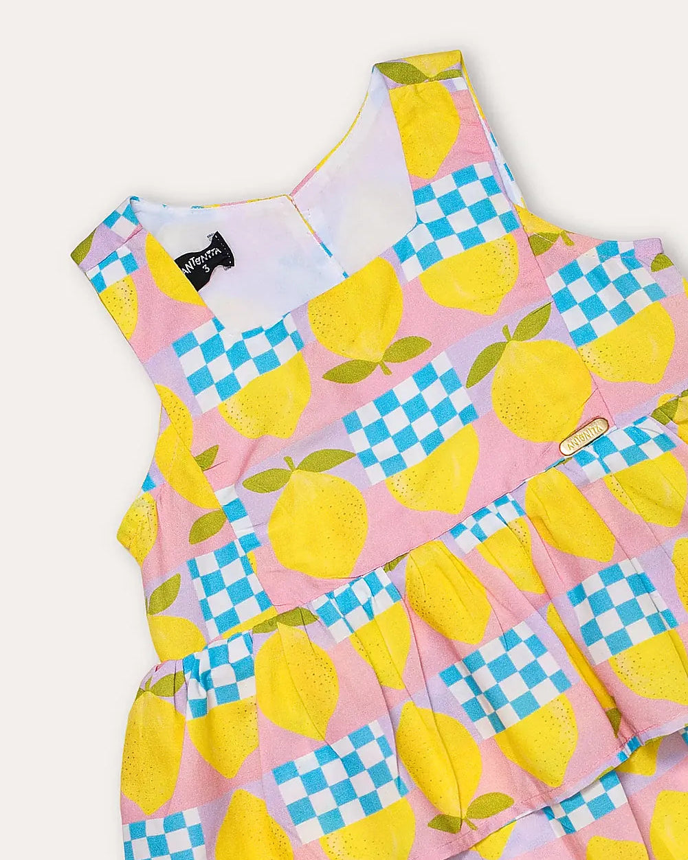 Macacão feminino infantil com estampa de limões e quadrados coloridos, alças largas e saia em camadas.