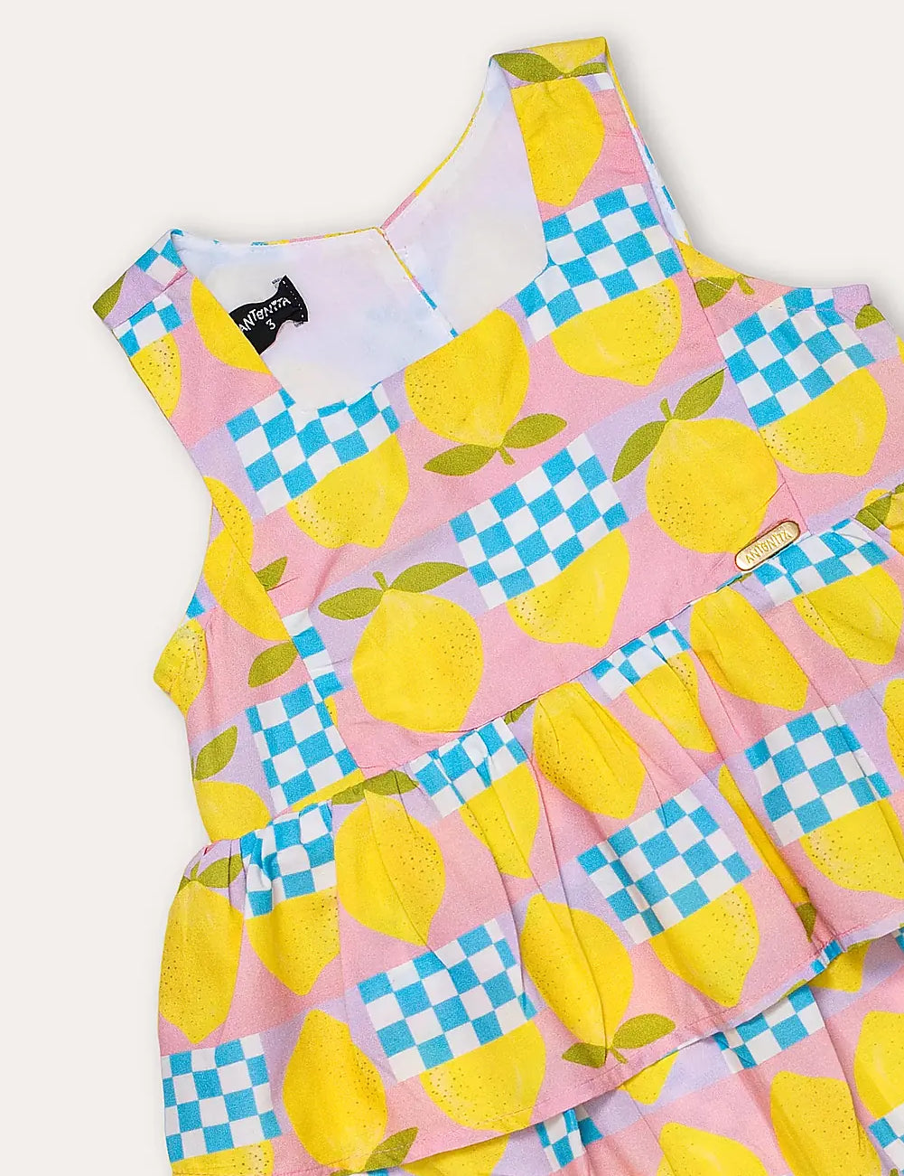 Macacão feminino infantil com estampa de limões e quadrados coloridos, alças largas e saia em camadas.