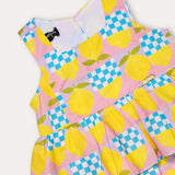 Macacão feminino infantil com estampa de limões e quadrados coloridos, alças largas e saia em camadas.